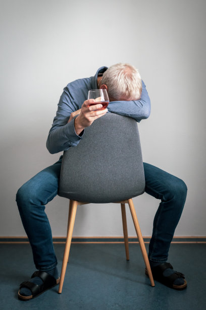 一个沮丧的人，头靠在胳膊上，手里拿着一只玻璃杯，坐在扶手椅上图片下载