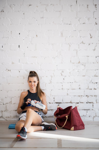 在跆拳道训练的间歇，一个年轻漂亮的女孩坐在墙边喝水图片下载