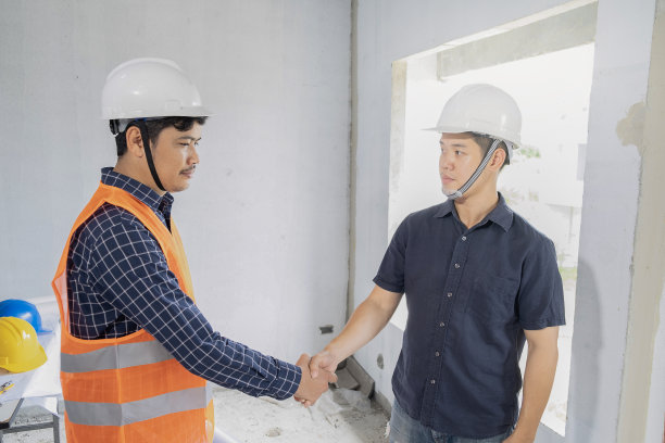 年轻的亚洲人与工头握手，在工地上向客户检查房屋，边看边指施工图片下载