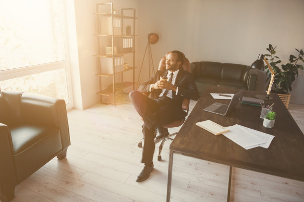 上面高角度看正面的美国黑人男子照片商人坐椅子拿外卖杯饮料看窗户想象成功穿着燕尾服在工作场所工作图片下载