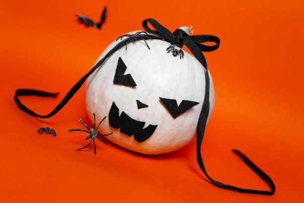 白色万圣节邪恶南瓜的肖像与黑色蝴蝶结的背景橙色或郁郁葱葱的熔岩颜色。图片下载