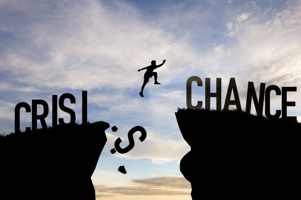 心态概念，剪影人跳跃从危机到机会的措词在云天和阳光的悬崖上。图片下载