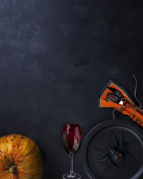 万圣节的概念是空的黑色盘子上有一个黑色的吓人的蜘蛛，万圣节南瓜，一个带有红色血污的酒杯和餐巾上的餐具在一个黑色的背景与复制空间。前视图。图片下载