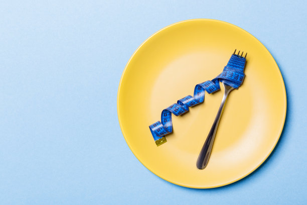 叉子的俯视图与测量卷尺在圆板上的蓝色背景。减肥概念与空空间为您的想法图片下载