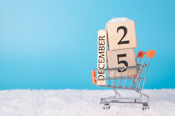 销售圣诞礼物的概念。玩具微型购物车的近距离照片满木制日历立方体车轮在白色雪蓝色的天空户外。空的空白图片下载