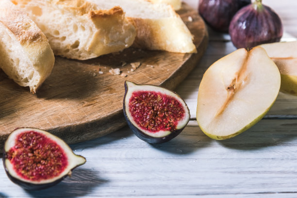 白木桌上放着法棍面包、无花果和梨。食物和膳食概念图片下载