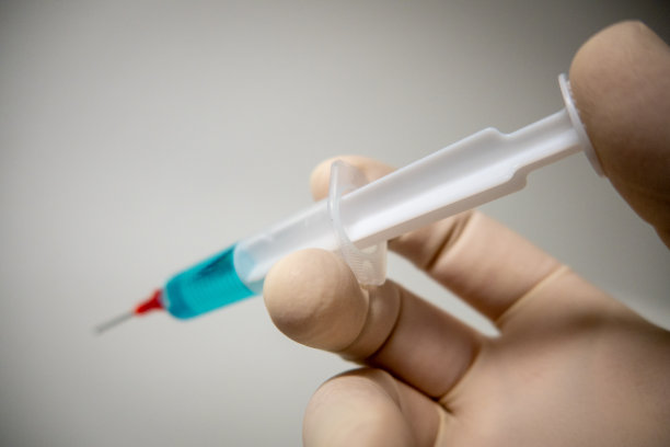 一只戴着手套的手拿着装有蓝色液体的医用注射器图片下载