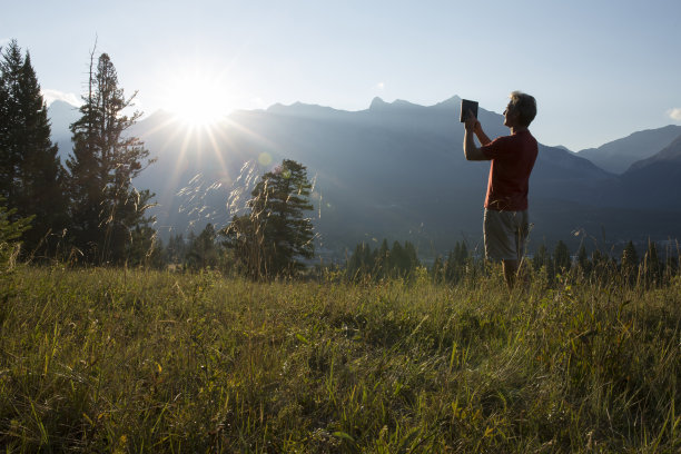 日出时分，一名男子在山区草地上用平板电脑拍照图片下载