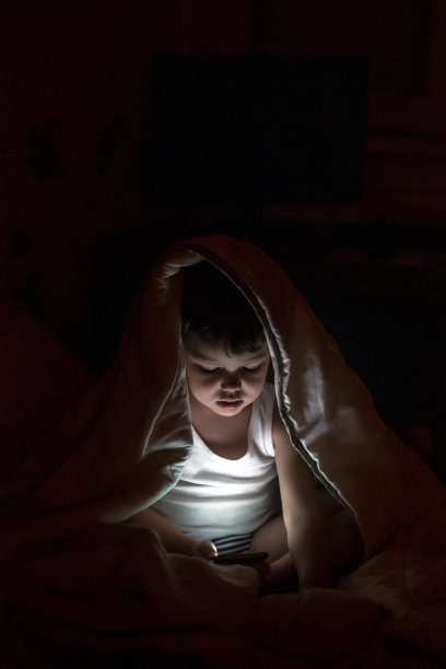 蹒跚学步的孩子，脸被手机屏幕照亮。图片下载