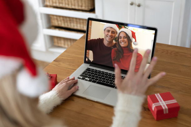后视图的女人在圣诞老人帽挥手，而有一个视频电话与夫妇在圣诞老人帽上的笔记本电脑图片下载