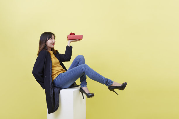 漂亮的亚洲女孩拿着礼物坐在白色的立方体上图片下载