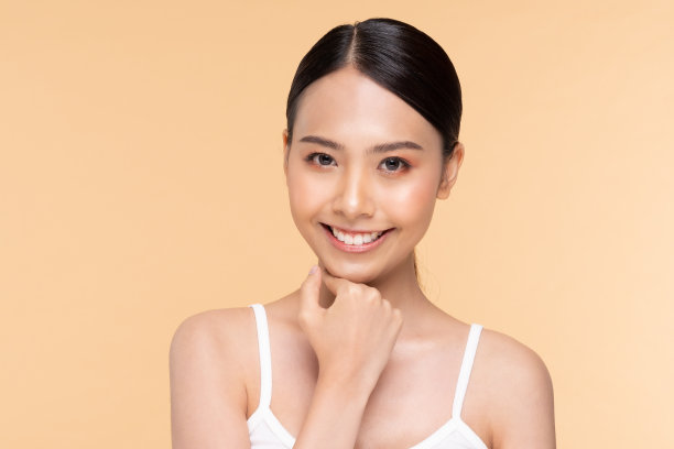 美丽的亚洲女人触摸下巴微笑，干净和新鲜的皮肤，幸福和愉快的情绪积极，米色背景，美容化妆品和水疗护理的概念图片下载