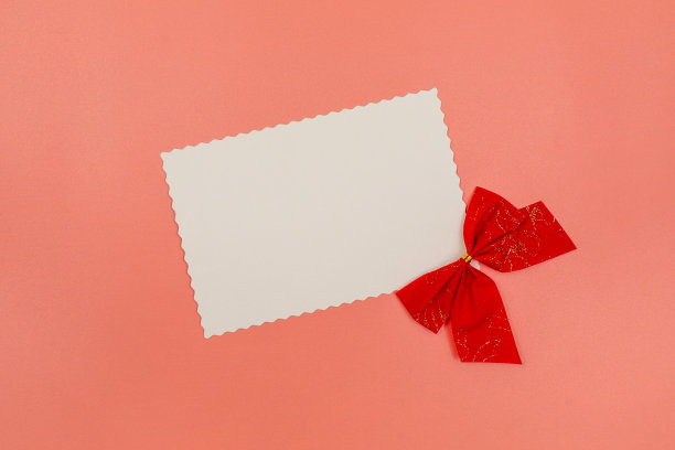 空白的白色明信片和红色蝴蝶结装饰在粉红色的背景。圣诞节、新年、情人节、国际妇女节或母亲节作文。平铺与拷贝空间。图片下载