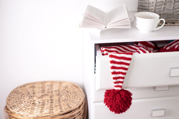 一顶戴着红色大绒球的白红帽挂在一个白色抽屉柜的打开的抽屉里图片下载