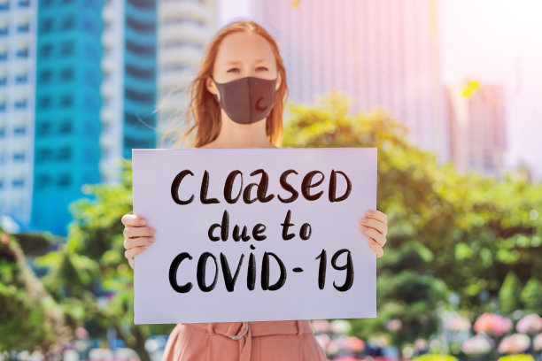 戴医用口罩预防冠状病毒疾病的妇女举着一幅海报，因Covid-19而关闭。手写文字-文字孤立在白色。冠状病毒COVID - 19概念图片下载