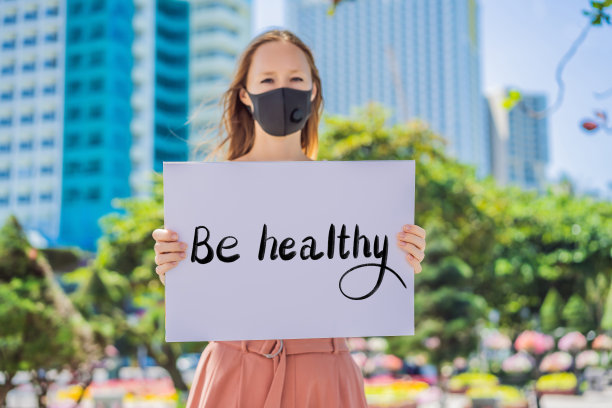 一名妇女戴着医用口罩预防冠状病毒病，手持海报BE HALTHY手写文字孤立在白色。冠状病毒COVID - 19概念图片下载