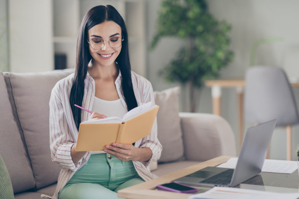 年轻开朗的商务小姐照片，拿着抄写本，笔，写字，戴眼镜，衬衫在家里的工作站室内图片下载