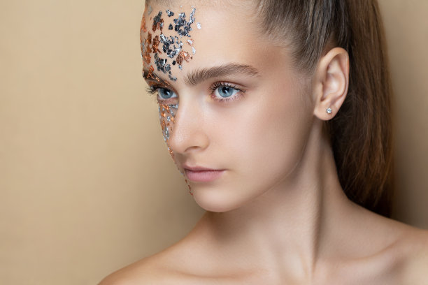 米色背景下的年轻美丽的女孩。特写肖像。黄金金属面图片下载