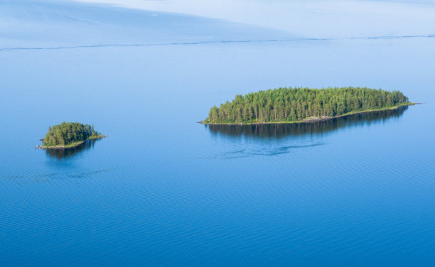 在阳光明媚的夏日，芬兰国家公园的湖泊景观与蓝色的水和美丽的松树岛图片下载