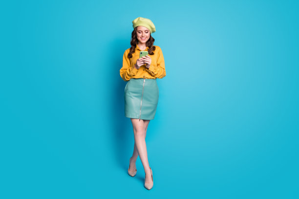 全尺寸照片的积极女孩博主使用智能手机跟随分享评论社交网络新闻穿黄色高跟鞋隔离在蓝色背景图片下载