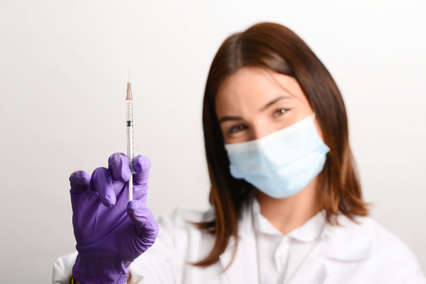 年轻护士手持装有疫苗的注射器，戴防护手套，穿着白大褂，隔离在白色背景上图片下载