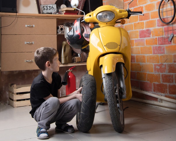 一个年轻的白人男孩非常专注，他自己捡起了他黄色摩托车上的一个轮胎。时尚的车间图片下载