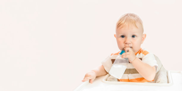 一个快乐的蓝眼睛的小孩正坐在桌子旁，用奶嘴喝着瓶子里的水。独立的。本空间图片下载