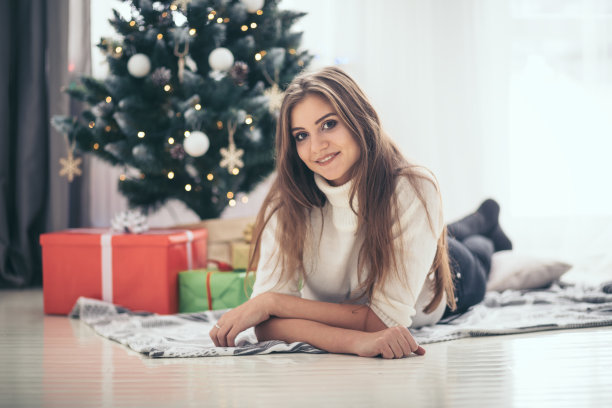 快乐的年轻女子躺在圣诞树前的地板上，周围摆满了圣诞礼物图片下载