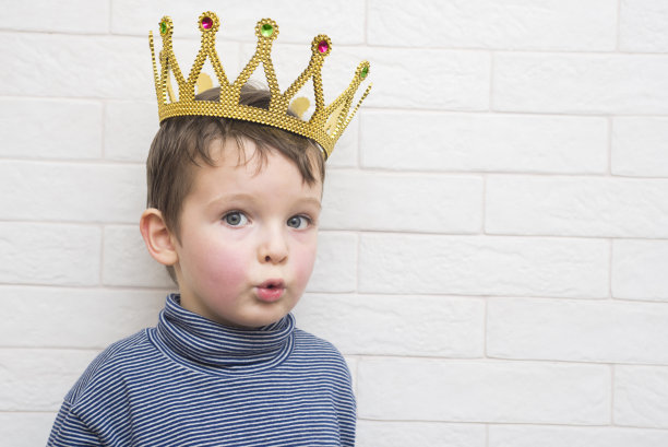 在砖墙背景下，一个头上戴着金冠的孩子图片下载