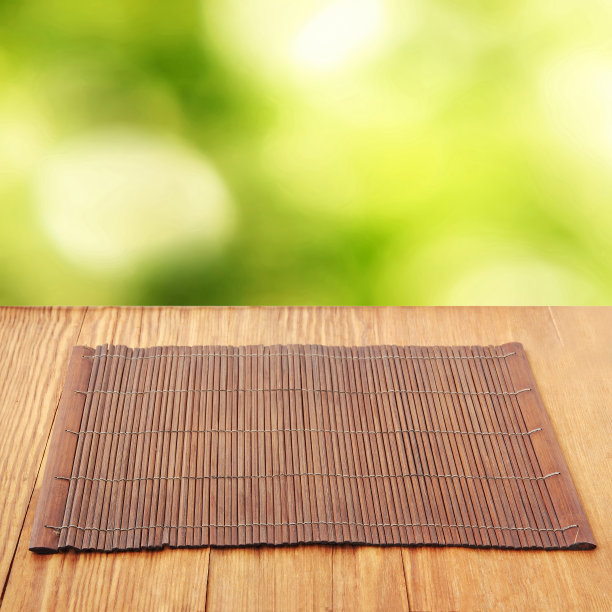 褐色的竹制食物垫放在木桌上，以散焦的绿色为背景。图片下载