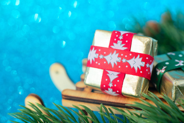 礼物躺在雪橇上靠近蓝色背景与发光散焦。有选择性的重点。放大照相的概念。圣诞节，冬季贺卡，海报。笔记本封面图片。新年快乐。图片下载