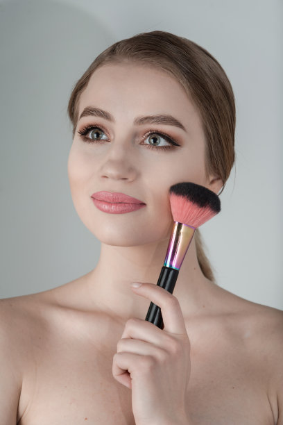 美丽的年轻女子在脸上搽粉图片下载