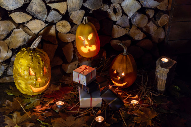 三个发光的南瓜和一串黑色和白色的礼物在秋天的树叶和蜡烛在万圣节之夜。图片下载