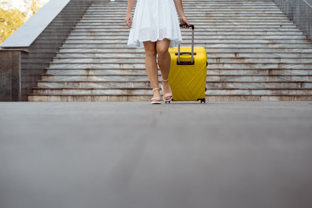 拿着行李箱的女孩走在街上。女性腿和黄色手提箱的特写。图片下载