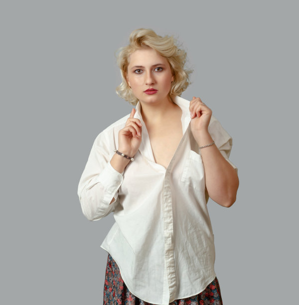 身穿白衬衫的金发女郎看着镜头，在灰色的背景下举起了他的衣领图片下载