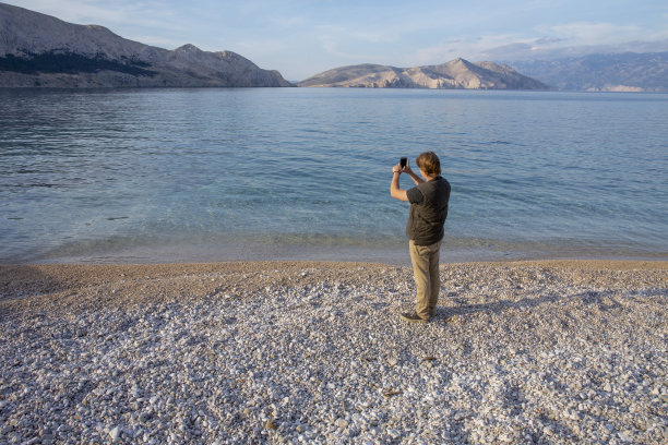 一个年轻人在海滩上用手机拍照图片下载