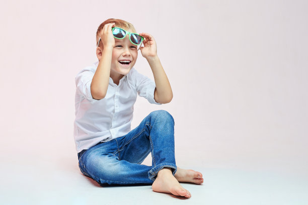 小男孩弯着腿坐着，举起眼镜，笑着把脸移开图片下载