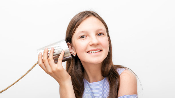 女孩微笑着把一个锡罐电话放在耳边，玩着复古的连在一起聊天。孩子孤立在白色背景上图片下载