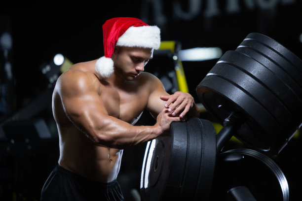 年轻肌肉发达的圣诞老人戴着圣诞帽，正在健身馆旁边的圆盘上锻炼肌肉休息图片下载