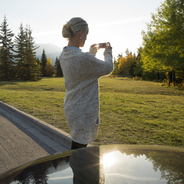 日出时分，妇女倚在停在乡村公路上的汽车上图片下载