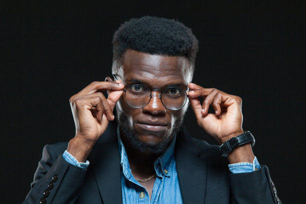 富有而严肃的黑皮肤商人正站在黑色的背景上调整他的眼镜图片下载