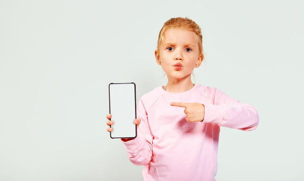 微笑的小漂亮的女孩在粉红色显示白色空白屏幕的手机文本空间隔离在白色背景。免费的广告空间。图片下载