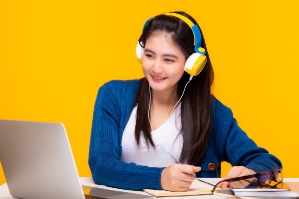 年轻的学生在网上看课，戴着耳机，她在家里学习。女学生听讲座，看网络研讨会，写笔记，看笔记本电脑，而老师则通过视频电话进行教学。遥远的教育图片下载