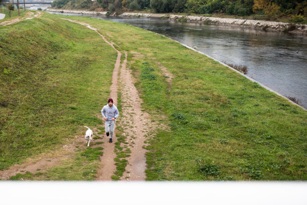 一个男人和他的狗在河边奔跑，鸟瞰图片下载