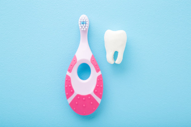 白色的牙齿和粉红色的婴儿牙刷在浅蓝色的桌子背景。柔和的颜色。婴儿牙齿卫生。特写镜头。自顶向下的观点。图片下载