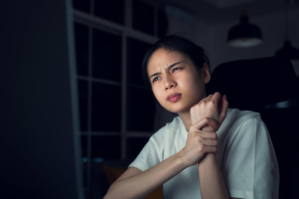 年轻的亚洲妇女有手腕疼痛，因为使用电脑打字和长时间在夜间办公室工作。图片下载