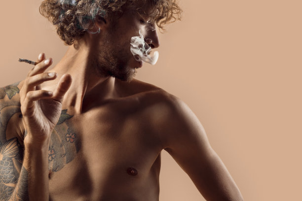 自由泳。男人卷头发，裸露上身孤立地站在包上抽着烟，看着一边沉思图片下载