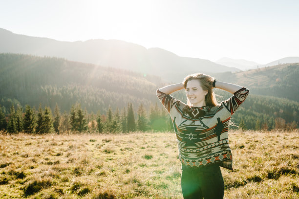 幸福的女人在秋日日落张开双手。时髦的年轻女孩在山顶享受日出。游客旅行者背景山谷。徒步旅行者在欧罗巴国家寻找阳光。图片下载