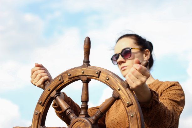 女孩控制着游艇，双手放在方向盘上，方向盘在天空背景上图片下载
