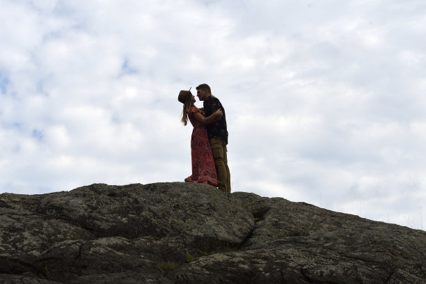 一对年轻夫妇的剪影相爱彼此拥抱，并即将亲吻沿着岩石海岸对一个穆迪的天空图片下载